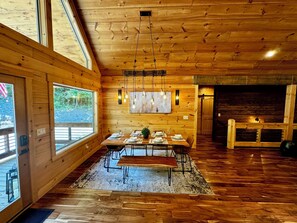 Un intérieur en bois comprenant un coin repas, de grandes fenêtres et une cheminée.