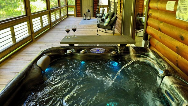 A hot tub with a wooden deck, two glasses of red wine, and a view of the forest. - Hidden Creek Cabin Sleeps 8 • Hot Tub • Game Room • 8 Min to Downtown (Blue Ridge)