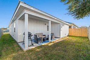 A white single-story house with a covered patio area featuring outdoor furniture and a grill.