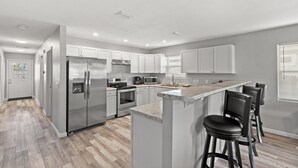 A modern kitchen with stainless steel appliances, white cabinetry, and a bar area with stools.