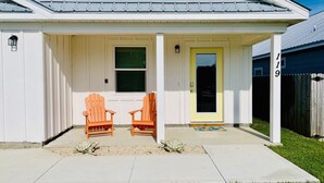 A white house with a yellow door, two wooden chairs, and a small turtle on the porch.