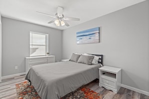A bedroom with a bed, nightstands, a ceiling fan, a window with blinds, and a painting on the wall.