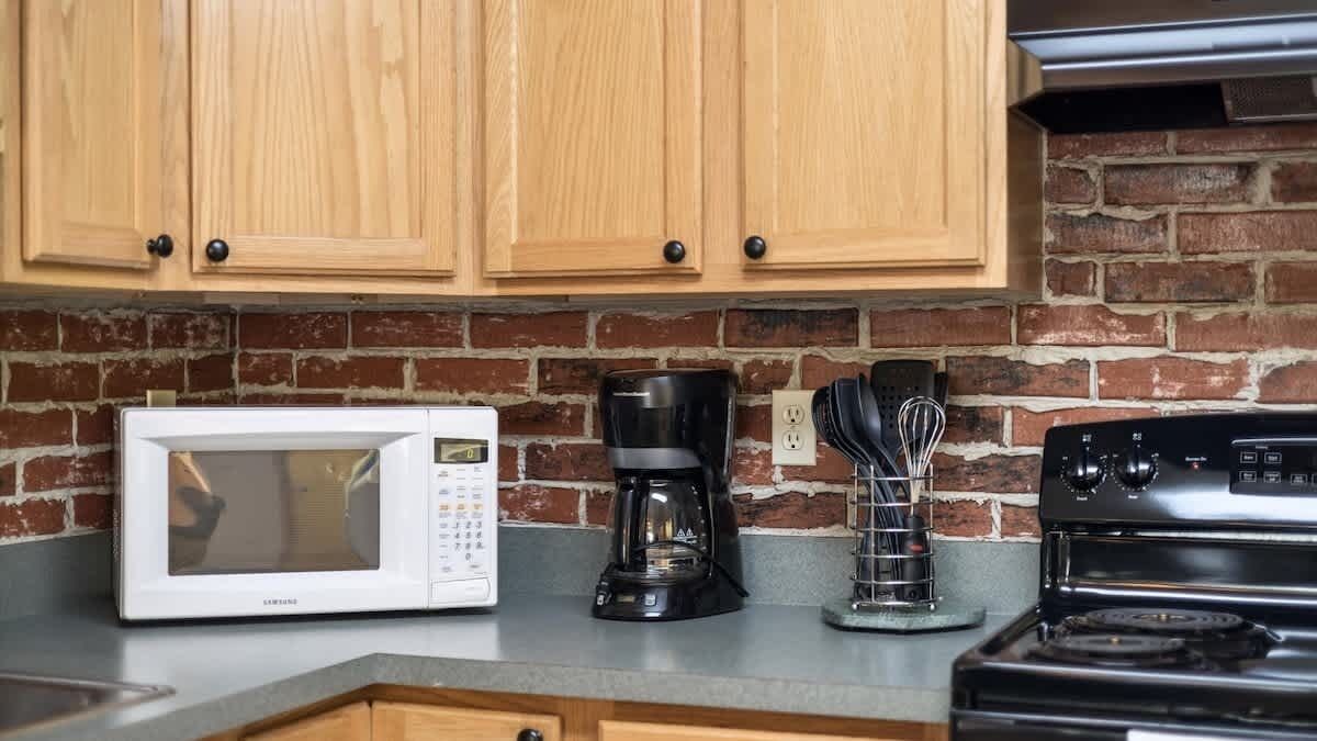 A kitchen with wooden cabinets, a white microwave, a black coffee maker, and a stove.
