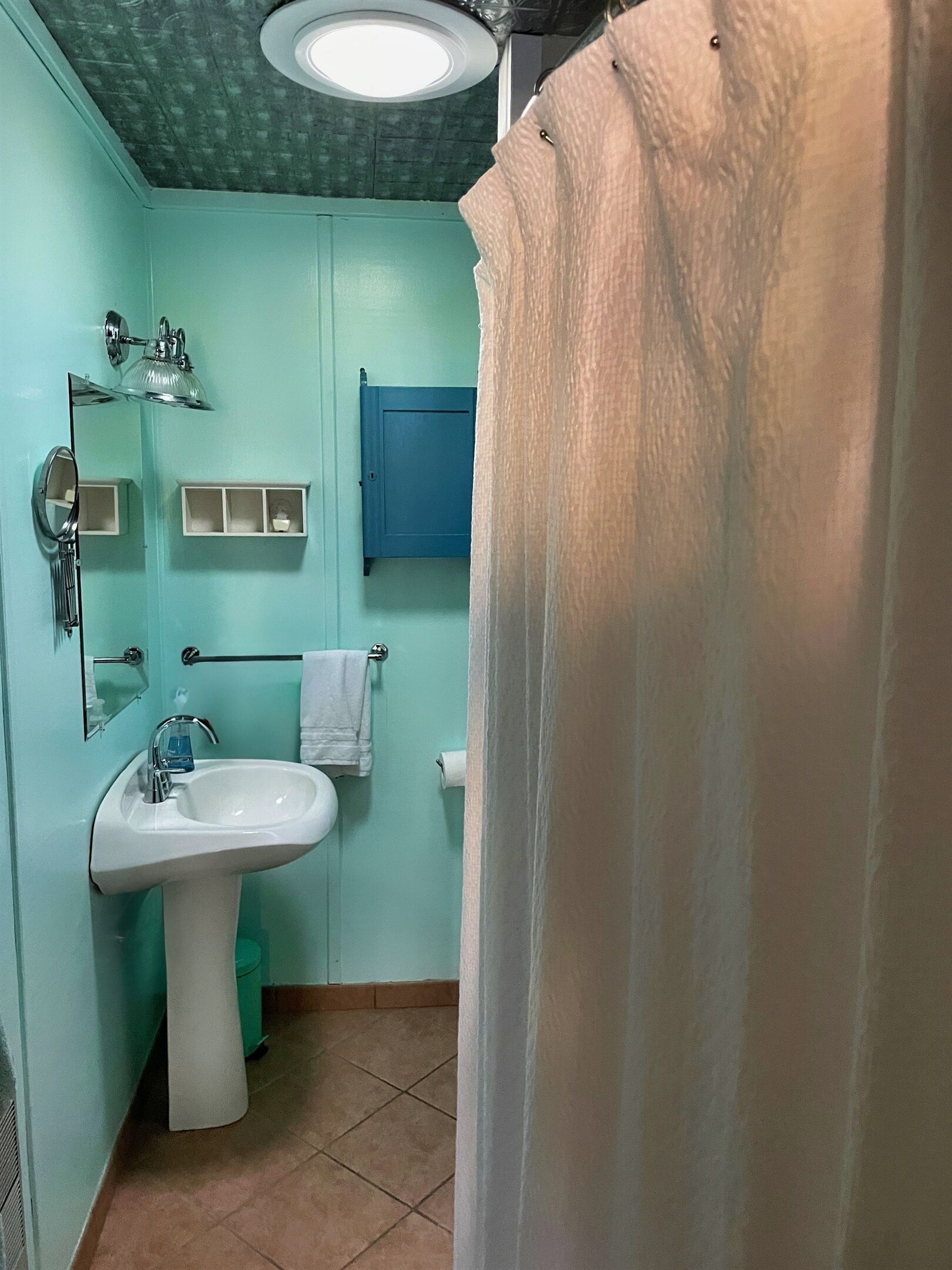 Un baño con un lavamanos blanco, un espejo, un armario azul y una cortina de ducha.