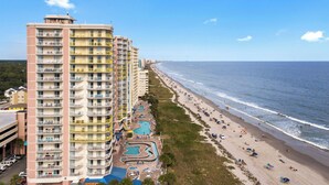 A high-rise hotel with multiple balconies, a beach, and a swimming pool area.