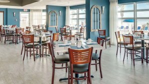 A spacious dining area with multiple tables and chairs, large windows, and a view of the outdoors.
