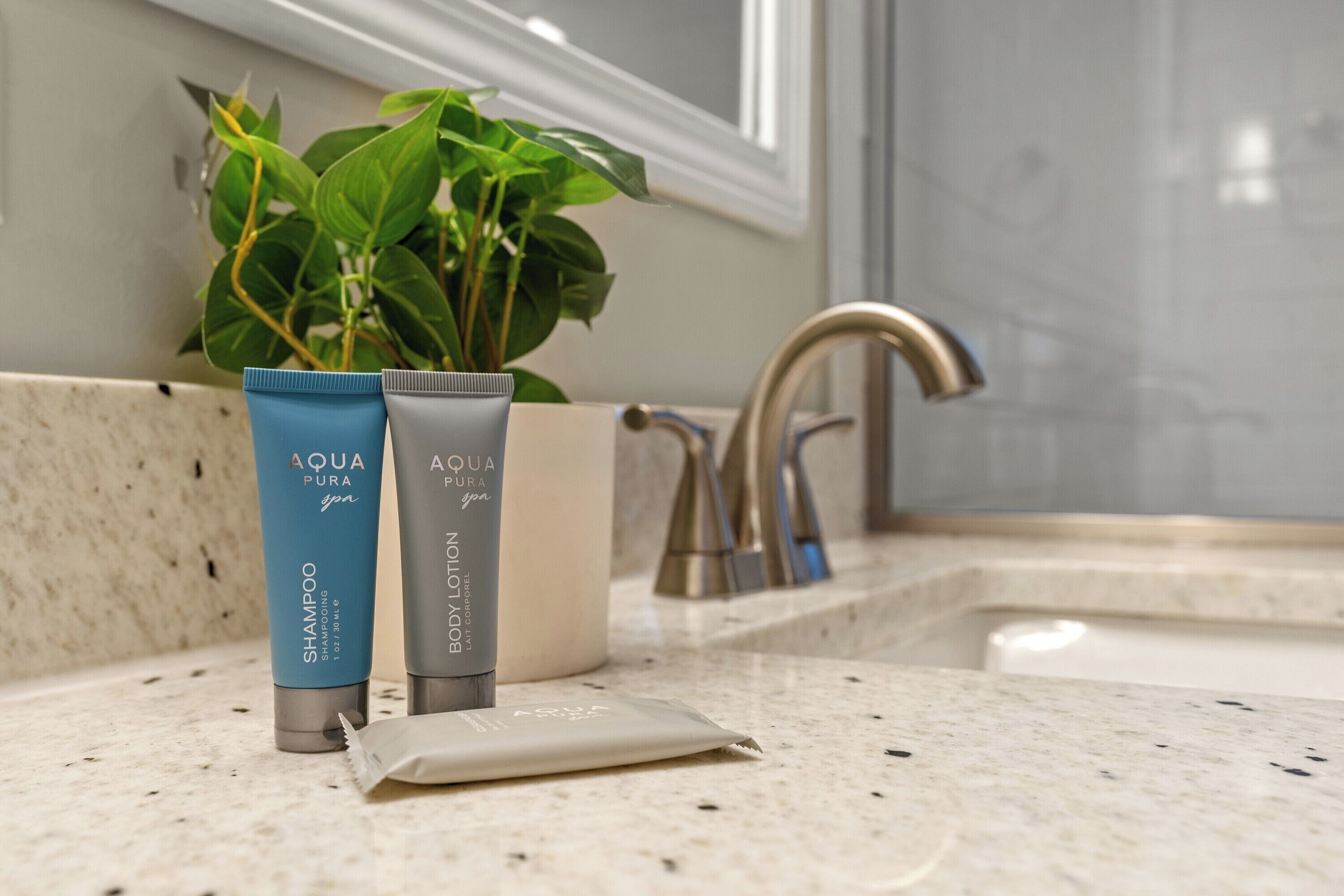 Un meuble-vasque de salle de bain avec une plante, deux flacons de shampoing et de lotion pour spa de la marque AQUA PURA, et un petit paquet.