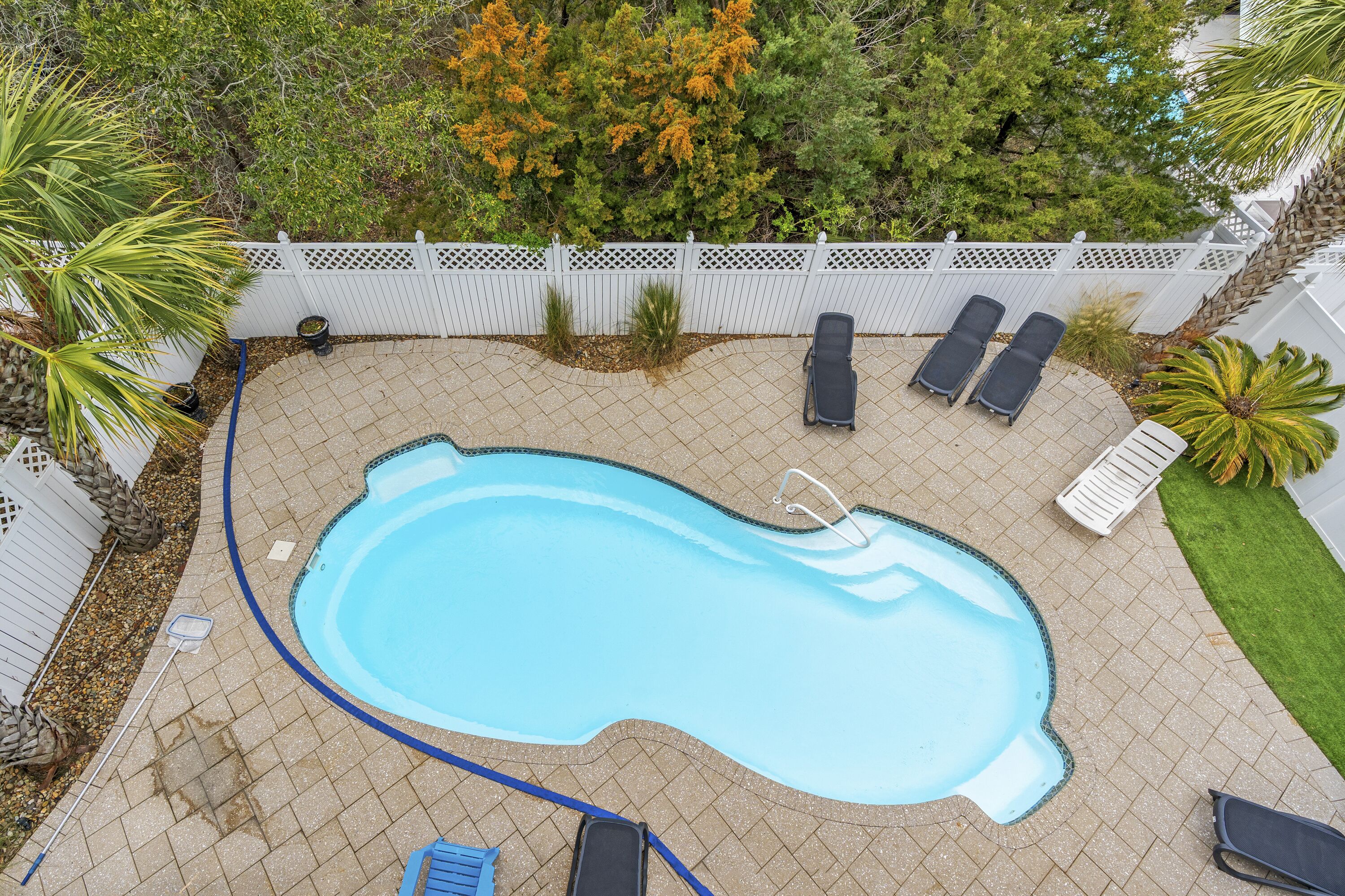 Une piscine rectangulaire entourée d’une clôture blanche et de chaises longues.