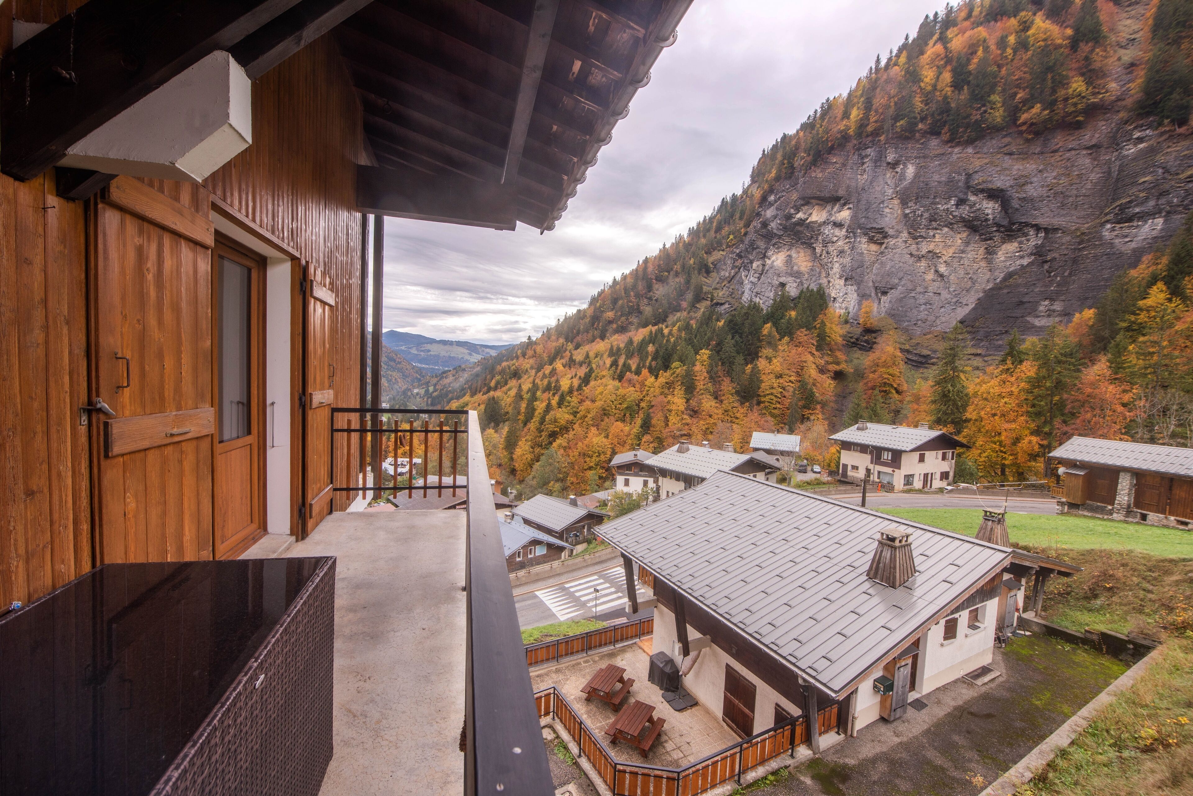 A wooden building with a balcony overlooking a valley with autumn-colored trees and a rocky mountain.