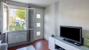 Ein modernes Wohnzimmer mit einem großen Flachbildfernseher, einem weißen Schrank und einem Fenster mit Blick ins Freie.