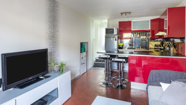 Eine moderne Küche mit roten Schränken, einem grauen Sofa und einem Flachbildfernseher.
