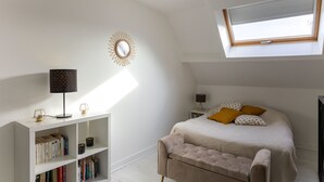 Ein Schlafzimmer mit Oberlicht, einem Bett mit Kissen, einem Nachttisch, einer Lampe und einem Bücherregal.