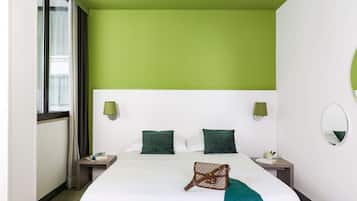 Une chambre d’hôtel avec un mur d’accent vert, un grand lit avec une literie blanche, deux tables de chevet avec des lampes et un miroir au mur.
