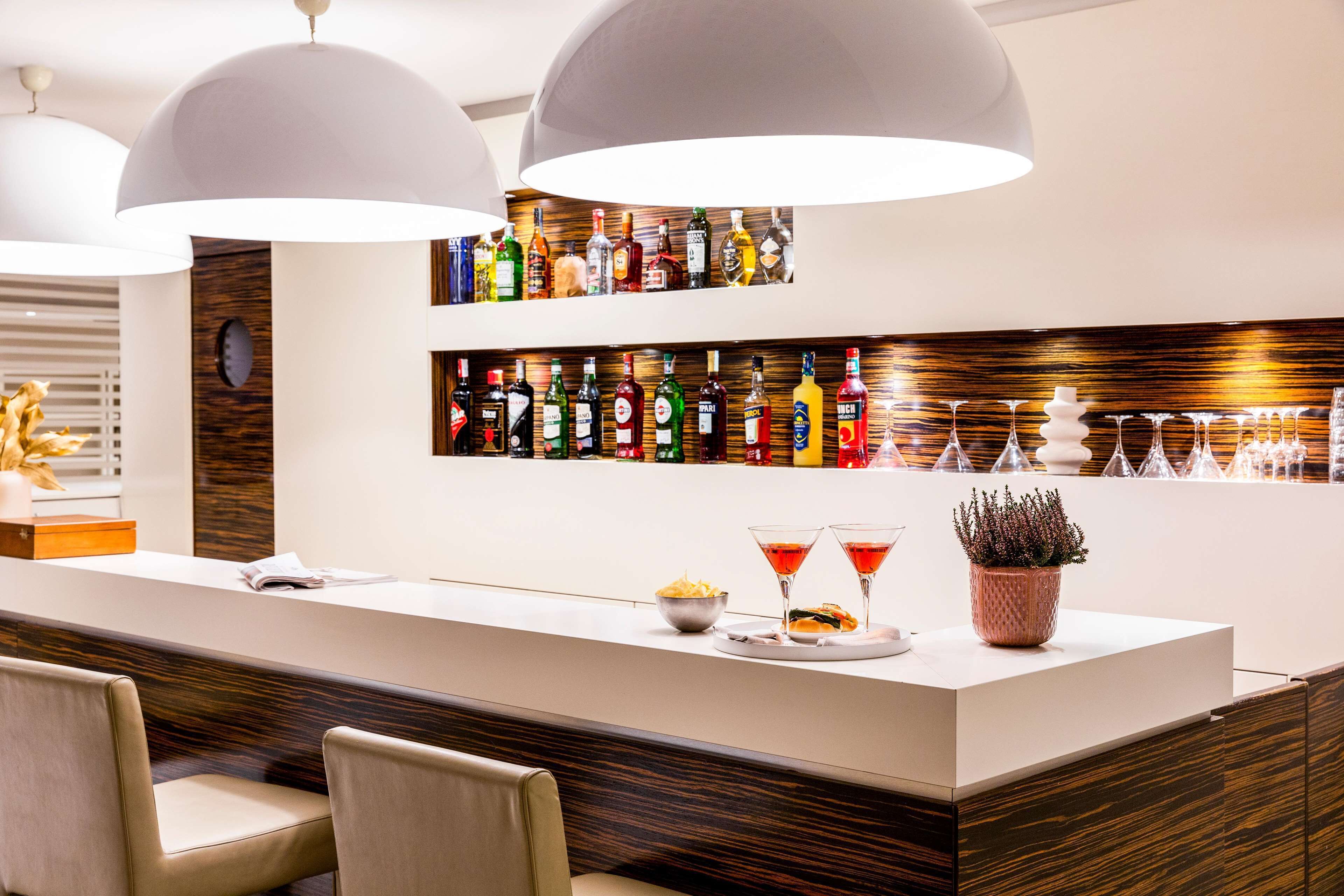 A bar area with a long counter, multiple bottles of liquor, and a few glasses.
