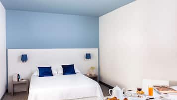 Une chambre d’hôtel avec un lit, des tables de chevet et une table pour le petit-déjeuner avec des croissants, du café et du jus de fruits.