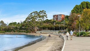Una platja amb un passeig marcat per corbes, un edifici al fons i arbres.