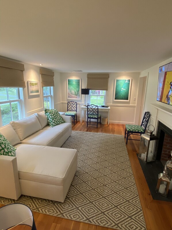 A modern living room with a white sofa, green patterned pillows, a geometric rug, and a fireplace. - Pristine Chatham home walkable to town, CBI, Fish Pier and baseball field (Chatham)