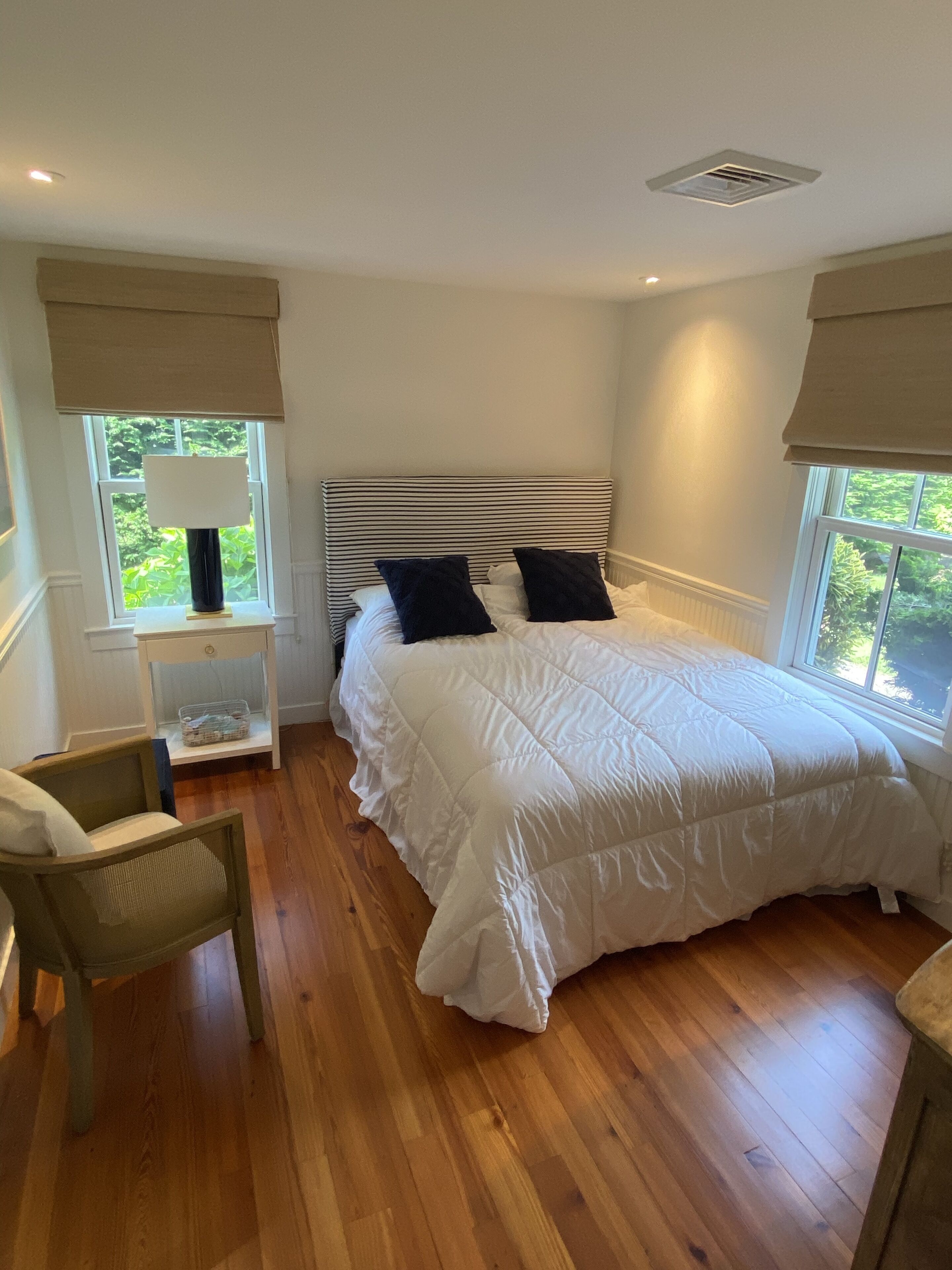 Une chambre avec un grand lit, une table de chevet, une chaise et une fenêtre donnant sur un paysage verdoyant.