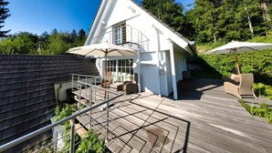 A modern house with a wooden deck, outdoor seating, and a covered patio area. - Holiday home mountain idyll (Sasbachwalden)