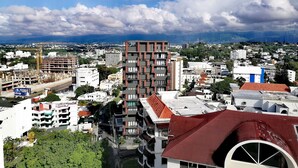 A high-rise building with multiple balconies and a red roof, surrounded by other buildings and greenery.