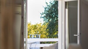 A bedroom with a bed, a chair, and a table. There is a balcony with a view of trees and a railing. - Villa Claire à Andernos - sea view with heated poo (Andernos-les-Bains)