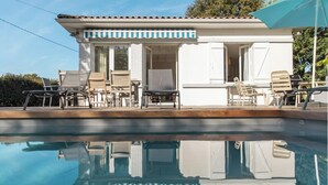 A poolside area with a white building, outdoor seating, and a clear view of the pool. - Villa Claire à Andernos - sea view with heated poo (Andernos-les-Bains)