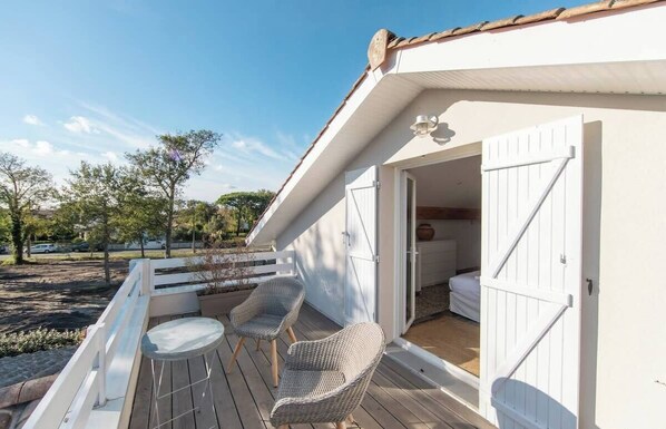 A white building with a balcony, two wicker chairs, and a small table.