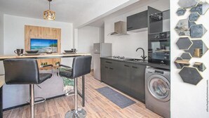 Une cuisine moderne dotée d’un îlot central, d’un lave-linge et d’un coin repas avec des tabourets de bar.
