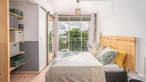 Une chambre à coucher avec un lit, une tête de lit en bois et un balcon donnant sur un paysage verdoyant.