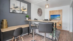 Une cuisine moderne avec un plan de travail en bois, deux tabourets de bar, un luminaire suspendu et une horloge murale.