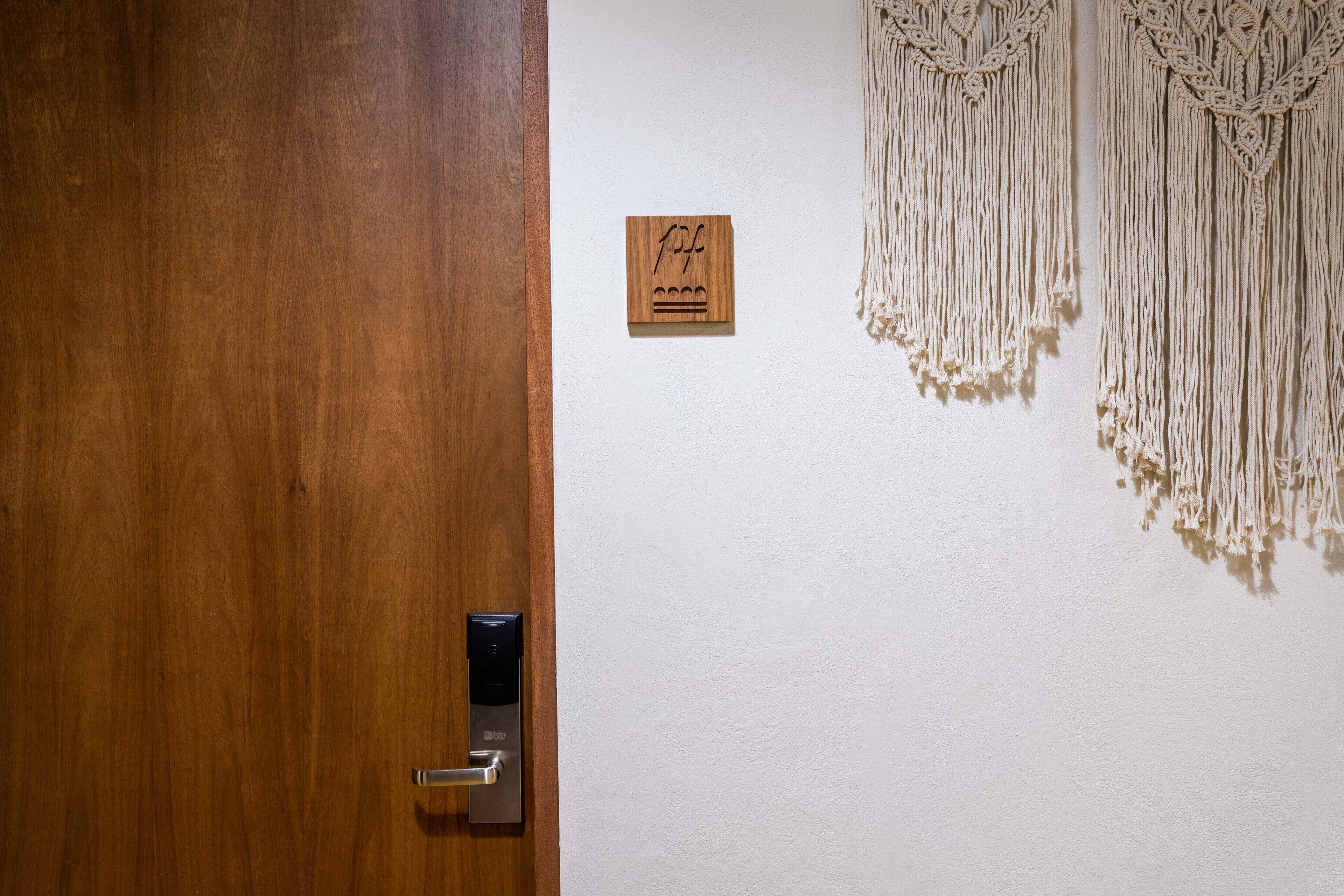 Una puerta de madera con una cerradura moderna, una pequeña placa de madera con un símbolo, y tapices de macramé en la pared.