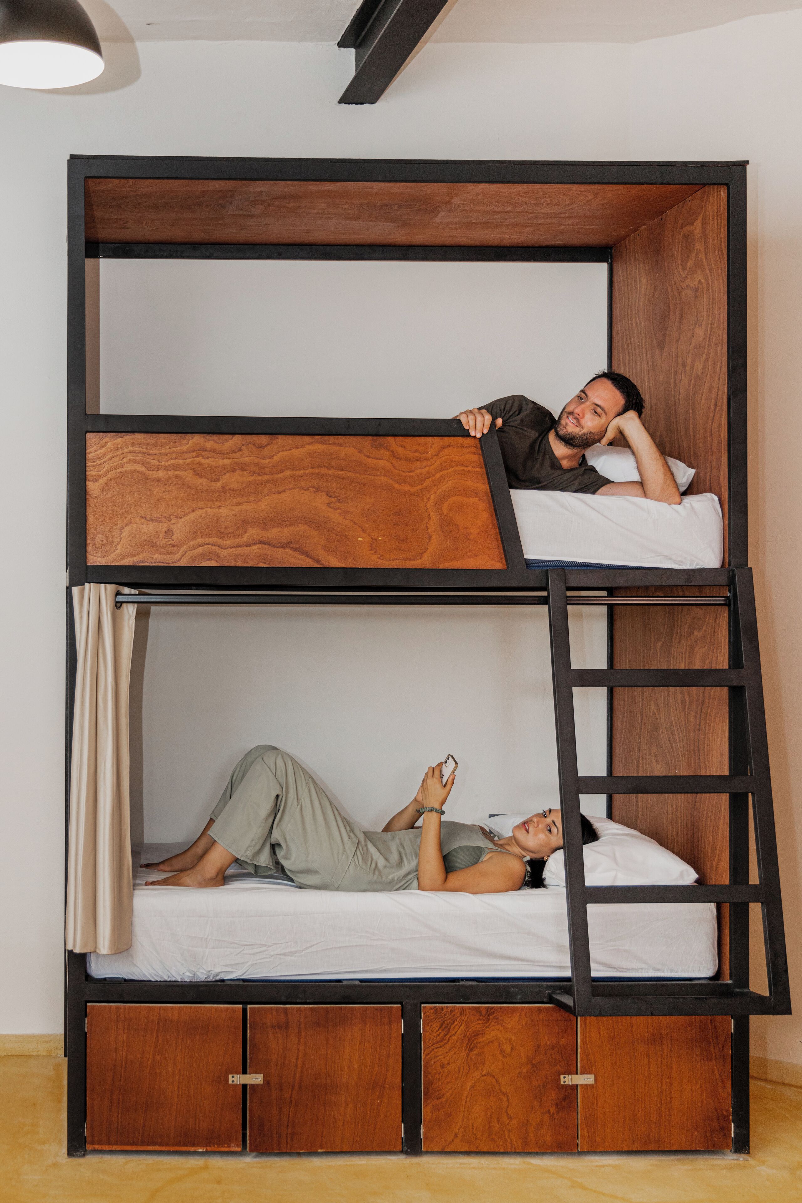 Una cama litera con estructura de madera, una escalera, dos camas y un pequeño armario.