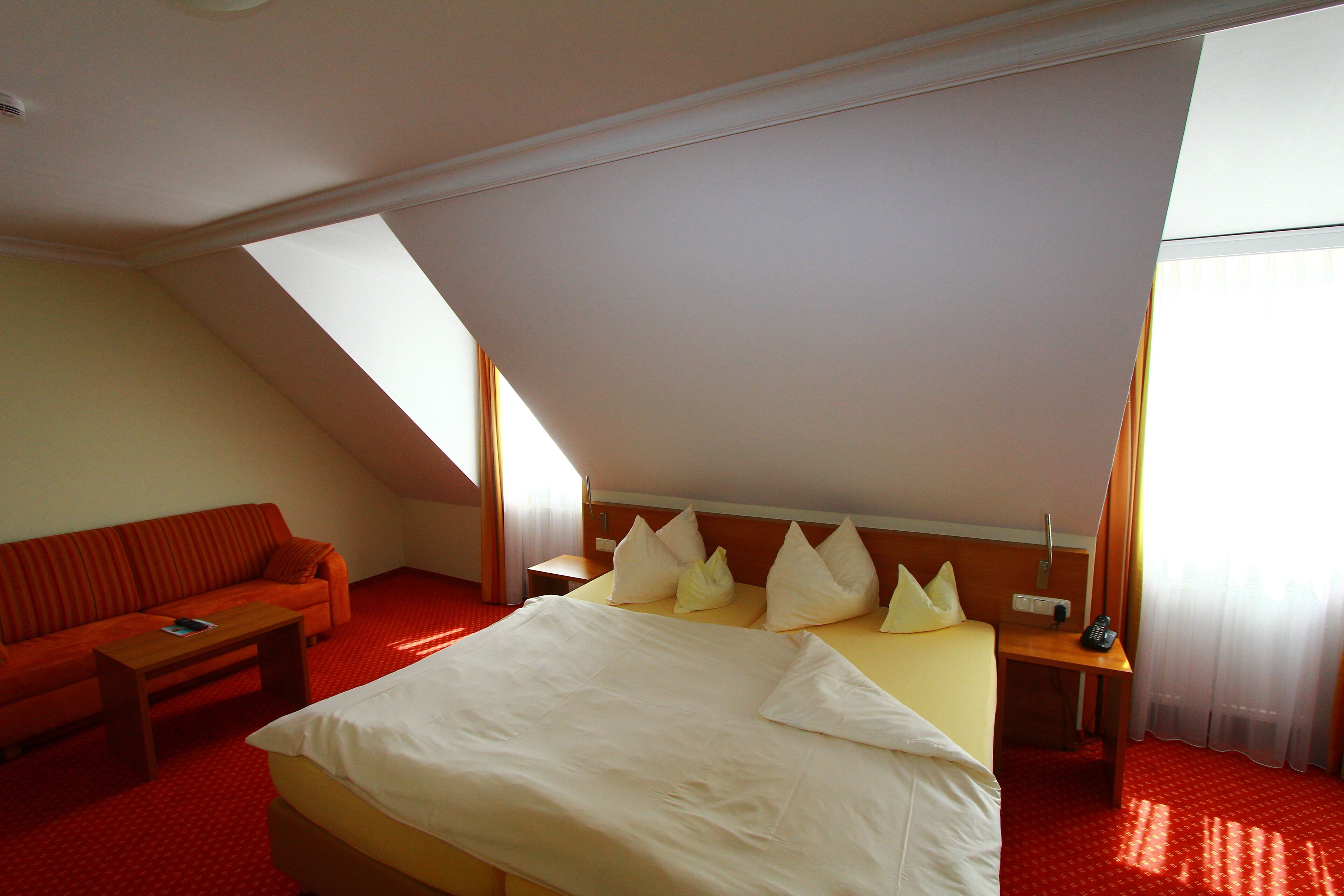 A hotel room with a bed, a sofa, a small table, and a nightstand with a lamp.