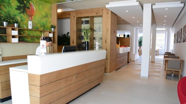 A reception area with a wooden reception desk, a counter, and a wall with shelves and plants. - Nar Hotel (Trebinje)