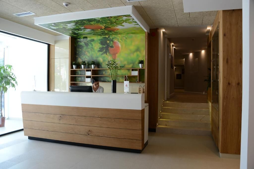 A reception desk with a wooden finish, a mural of a fruit tree, and potted plants.
