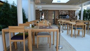 A restaurant with wooden tables and chairs, a glass wine bottle, and a wine glass on the table. - Nar Hotel (Trebinje)