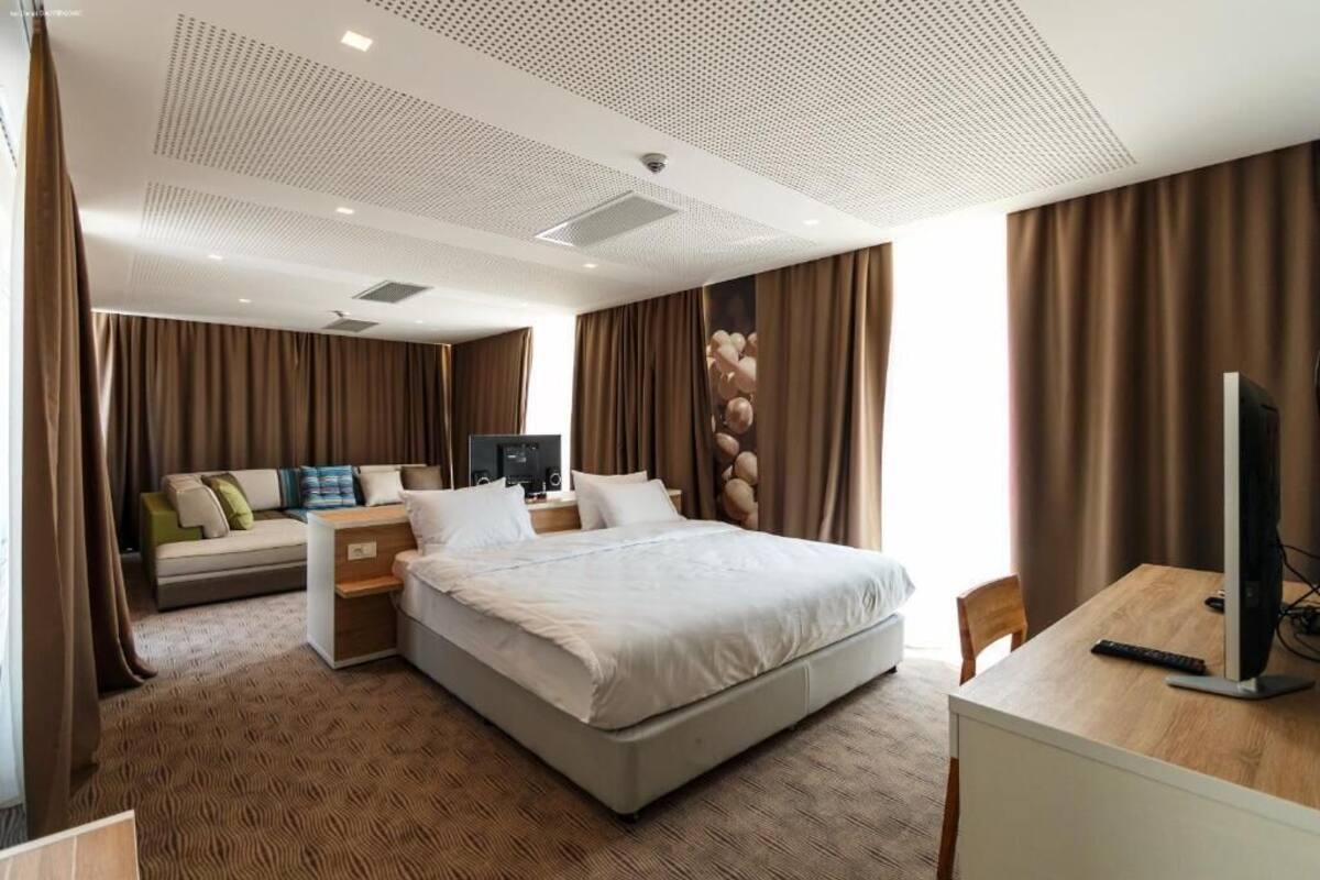 A modern hotel room with a large bed, a desk with a computer, a sofa, and a TV.