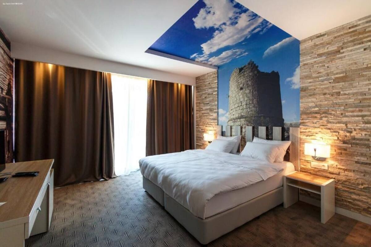 A modern hotel room with a large bed, a desk, and a stone wall mural.