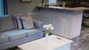 Un soggiorno con divano, tavolino e un vaso di fiori, e un'area cucina sullo sfondo.