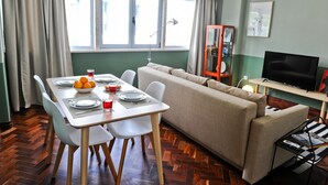 A dining area with a table set for four, a sofa, a TV, and a cabinet with a picture on the wall. - Negroni Balcony in Lisbon - by Misha s Place 1A (Lisbon)