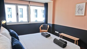 A hotel room with a bed, a chair, a bench, a lamp, and a window with a view of buildings. - Negroni Balcony in Lisbon - by Misha s Place 1A (Lisbon)