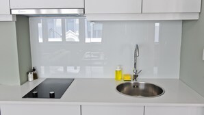 A modern kitchen with white cabinets, a stainless steel sink, and a black induction cooktop. - Negroni Balcony in Lisbon - by Misha s Place 1A (Lisbon)