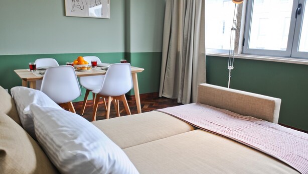 A hotel room with a bed, a desk with chairs, a window with curtains, and a wall with a painting. - Negroni Balcony in Lisbon - by Misha s Place 1A (Lisbon)