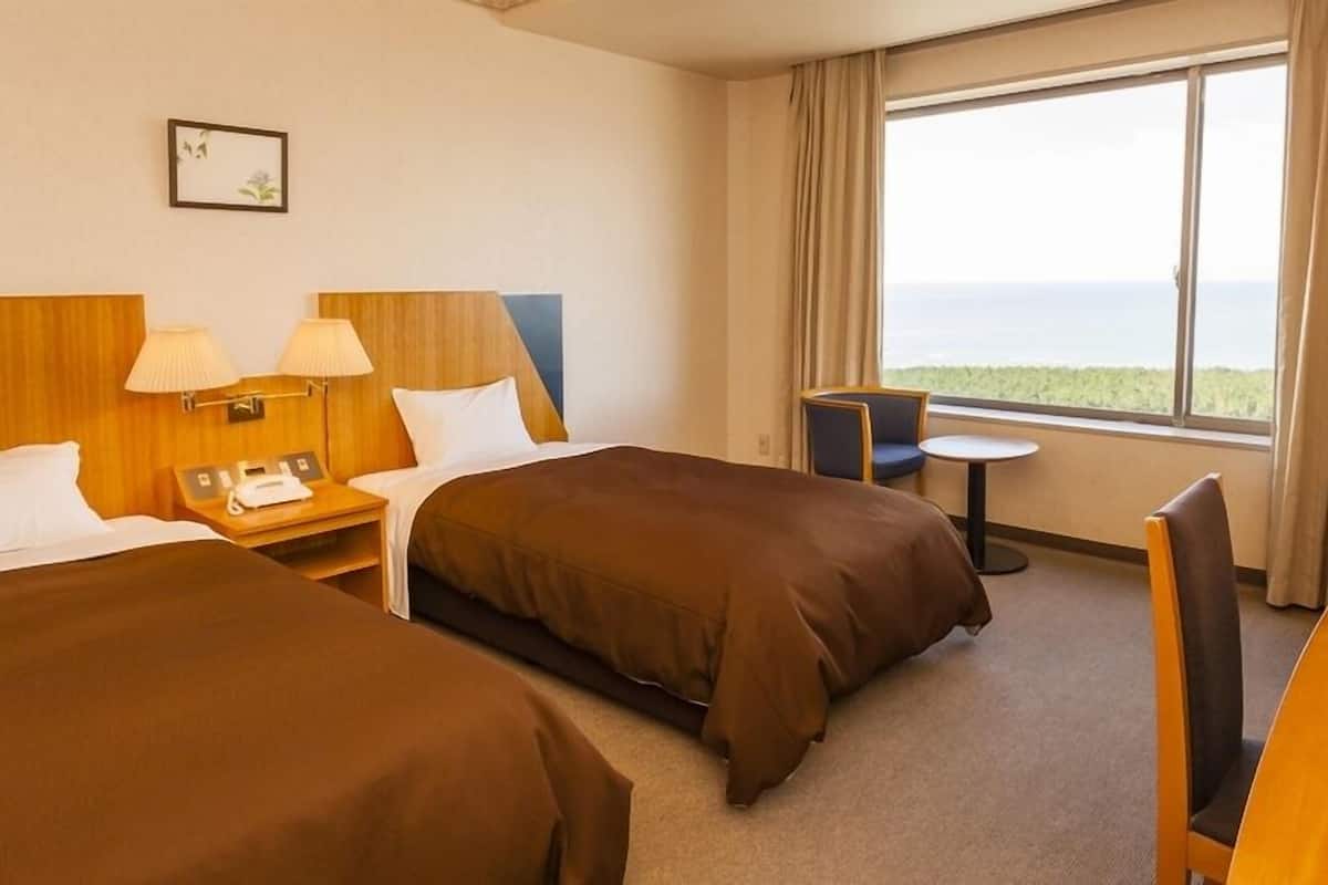A hotel room with two beds, a desk, a chair, a small table, and a window with a view.