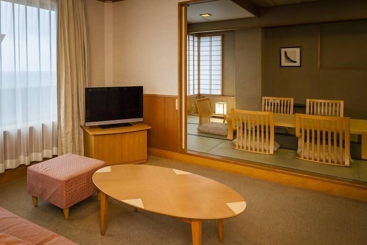 Ett hotellrum med en TV, en soffa, ett litet bord och utsikt över en matplats genom en glasvägg.