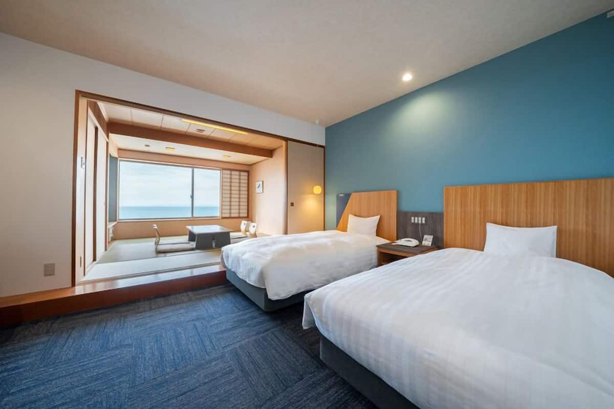 Ett hotellrum med två sängar, havsutsikt och en traditionell japansk skjutdörr.