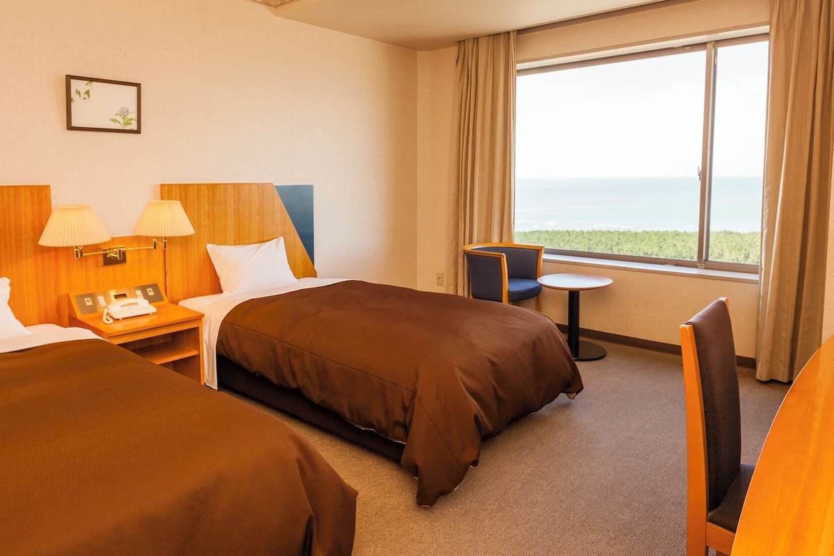 Ett hotellrum med två sängar, ett skrivbord med en telefon, ett litet bord och utsikt över havet.