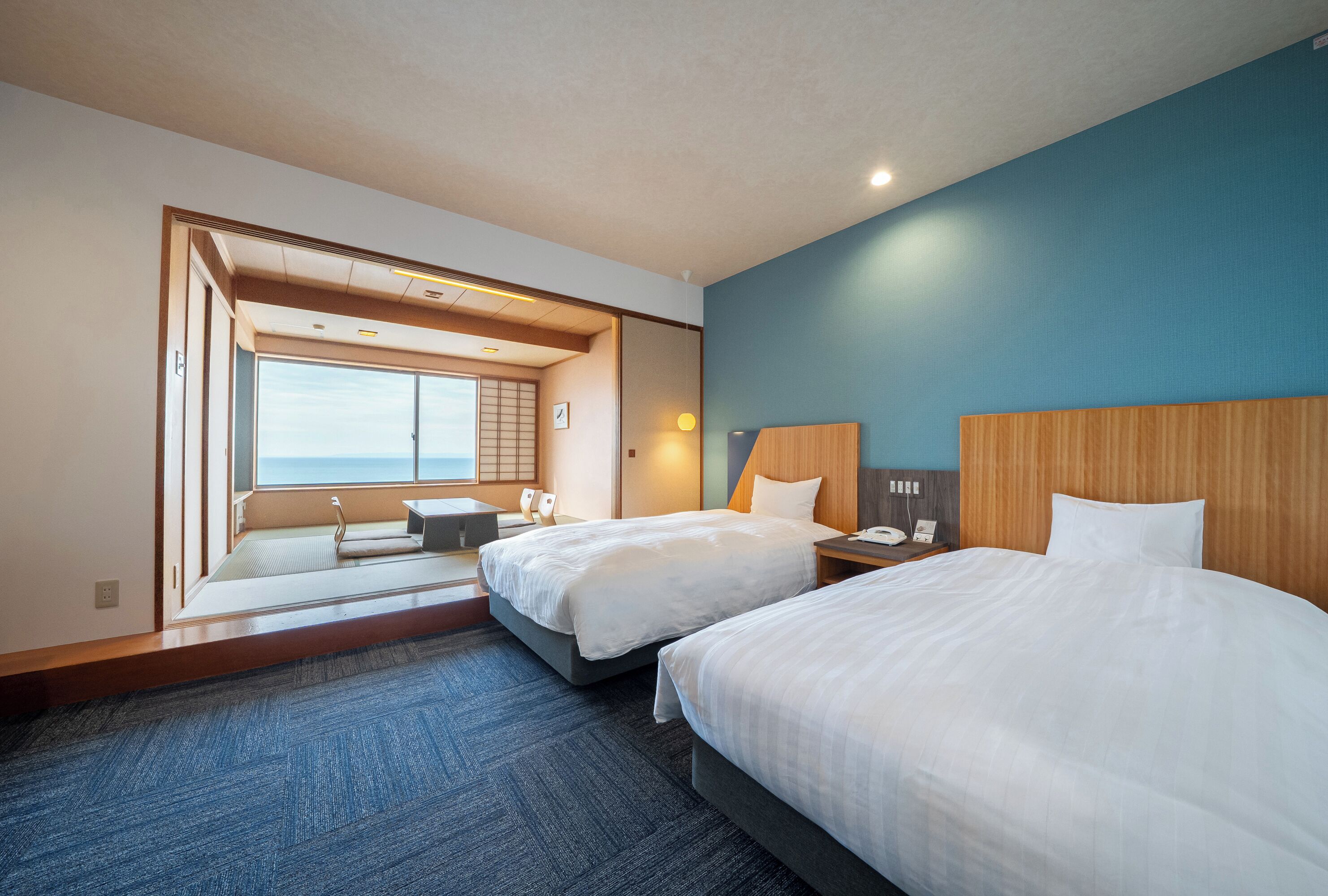 Et hotelværelse med to senge, udsigt til havet og en traditionel japansk skydedør.