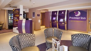 L'espace d'accueil d'un hôtel Premier Inn, comprenant un kiosque en libre-service, des comptoirs d'enregistrement et un coin salon avec des chaises à motifs.