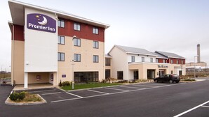Un hôtel avec une enseigne Premier Inn bien visible, un parking et, au fond, un bâtiment portant l’inscription « The Beacon ».